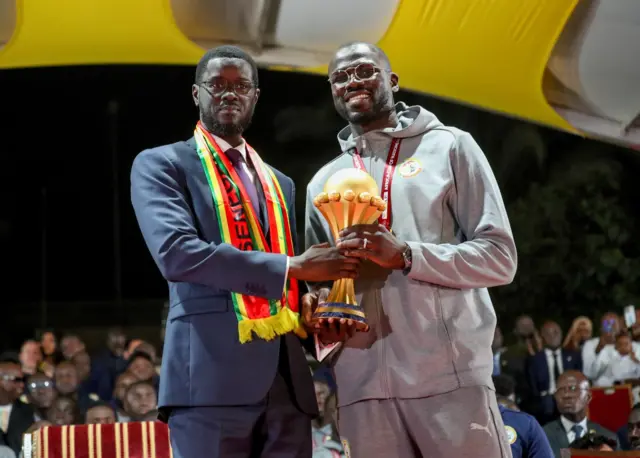 Le président sénégalais Bassirou Diomaye Faye et le capitaine de la sélection nationale, Khalidou Koulibaly, soulevant ensemble le trophée de la Coupe d'Afrique des Nations